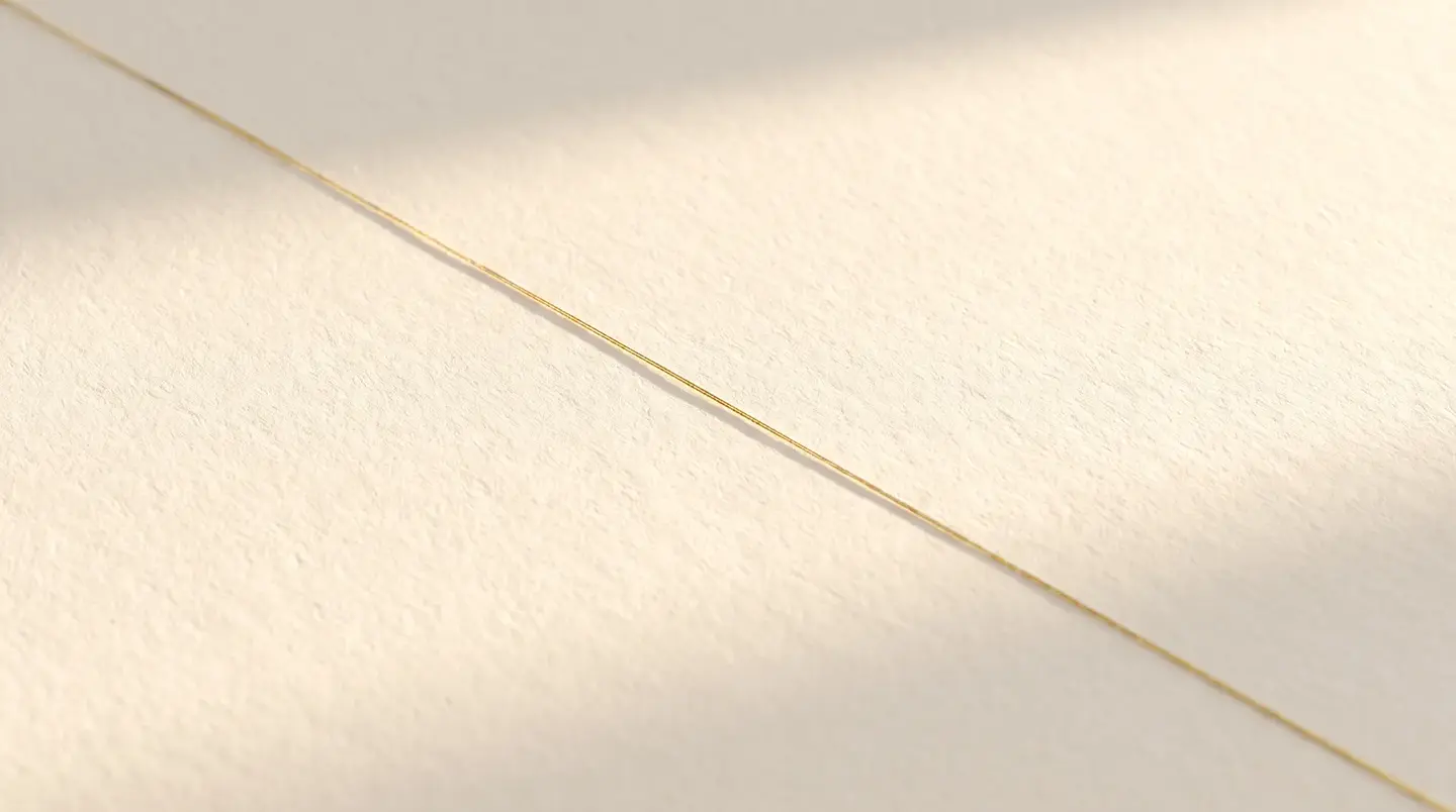A cream linen work surface lit from the side, a thin gold line of light crossing it