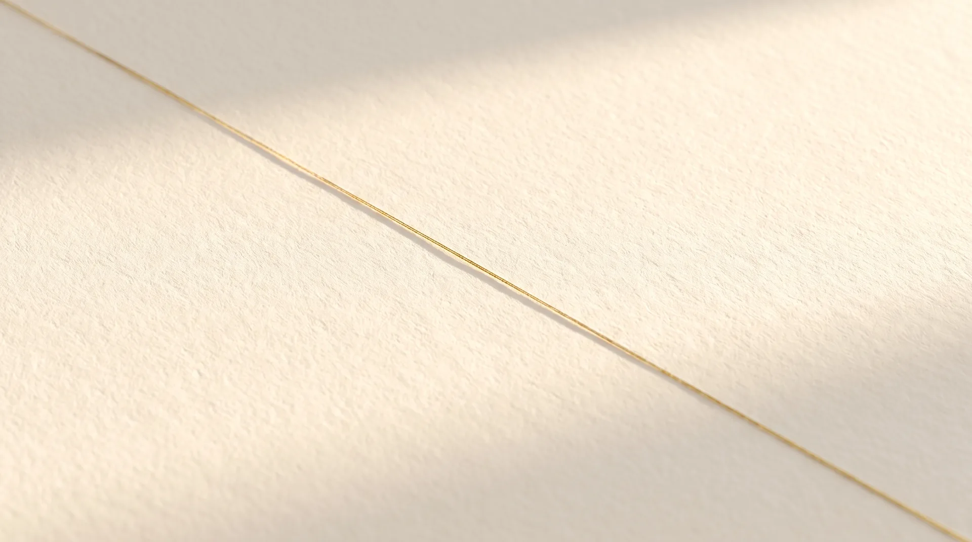 A cream linen work surface lit from the side, a thin gold line of light crossing it
